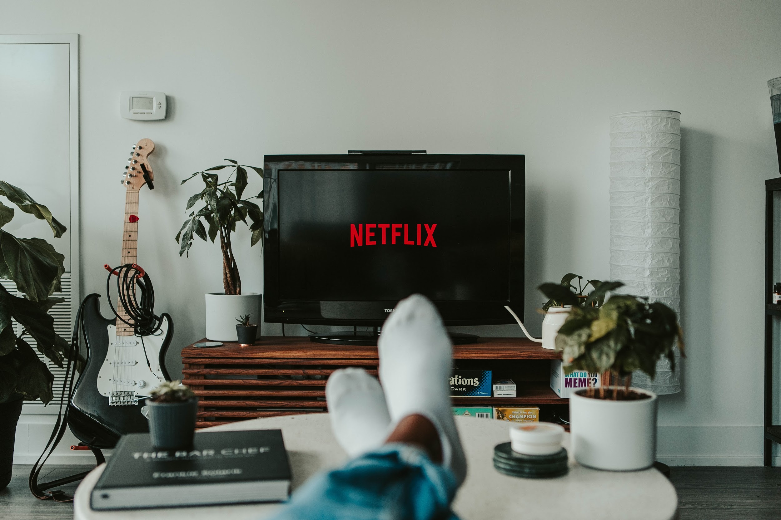 A picture of a pair of feet on a table in front of a TV with Netflix OTT network logo taken from the feet owner's perspective.